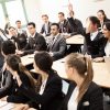 Portrait of business people in business school raising hands in training session